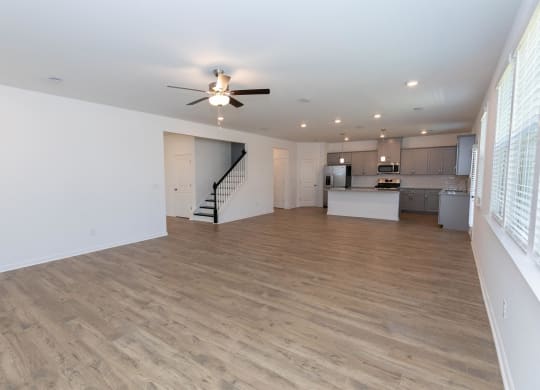 an empty living room with a ceiling fan and a kitchen