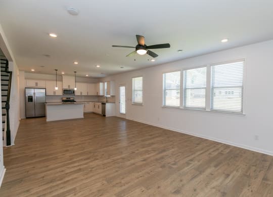 an empty living room with a ceiling fan and a kitchen