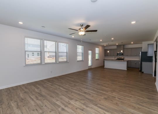 an empty living room with a ceiling fan and a kitchen