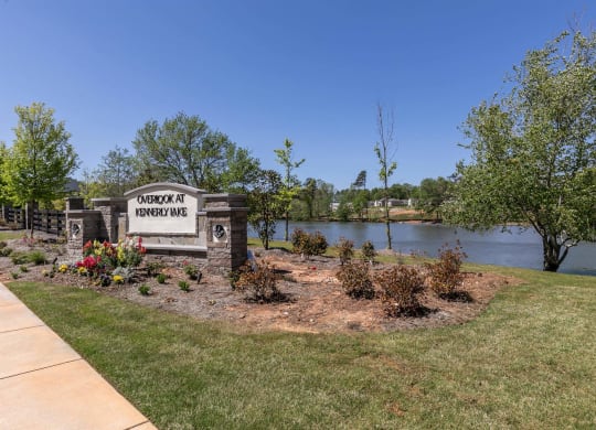 the subdivision is near a lake and has a sign for the subdivision on the lawn