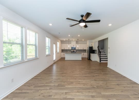 an empty living room with a ceiling fan and a kitchen