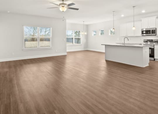 an empty living room with a kitchen and a ceiling fan