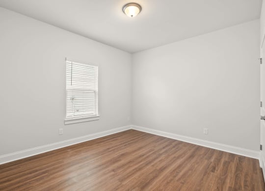 a living room with white walls and wood floors and a window
