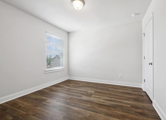 an empty room with white walls and wood flooring and a window