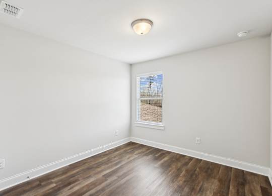 a living room with white walls and wood floors and a window