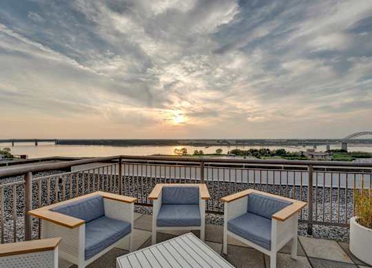 Two chairs and a table on a balcony overlooking a river at sunset.