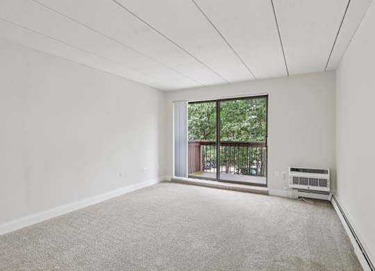 A room with a carpet floor and a window with a view of a balcony.
