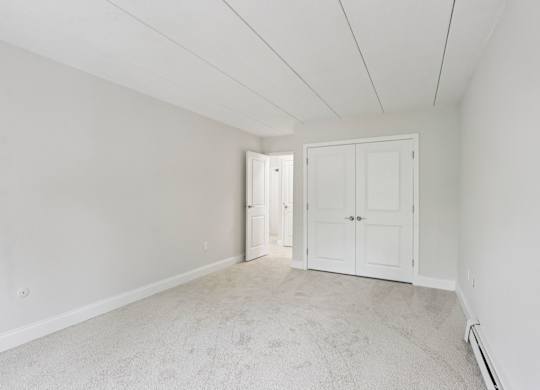 A room with white walls and carpeted floor with two doors.