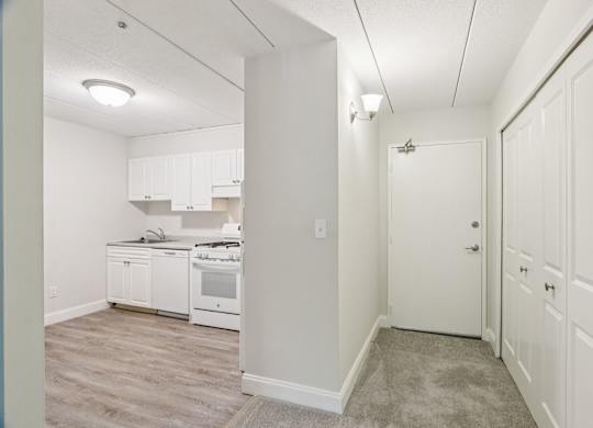 A kitchen with white cabinets and appliances in a room with a carpeted floor.