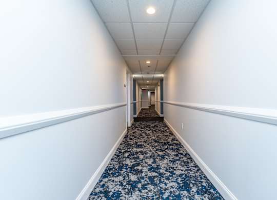 a long corridor with white walls and blue carpet