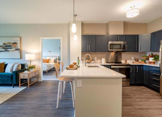 A sleek kitchen with quartz countertops, pendant lighting, and dark cabinetry equipped with stainless steel appliances.