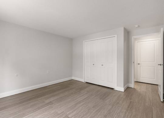 A room with white walls and wood flooring with two doors.