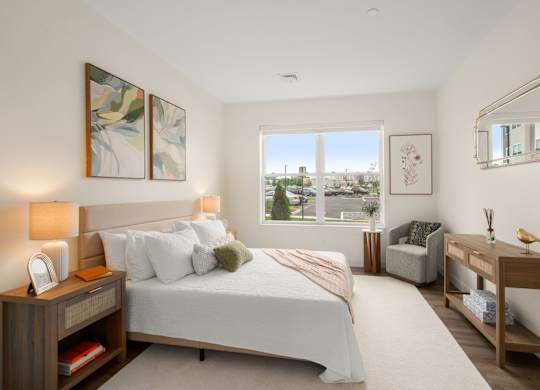 A bedroom with a large bed, a chair, a desk, and a window overlooking a cityscape.