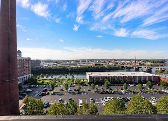 A tall red brick chimney is in the foreground of a parking lot with a large building in the background.