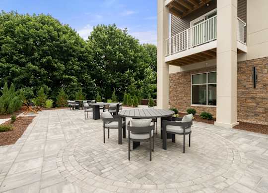 A patio with a table and chairs is surrounded by a stone wall and trees.