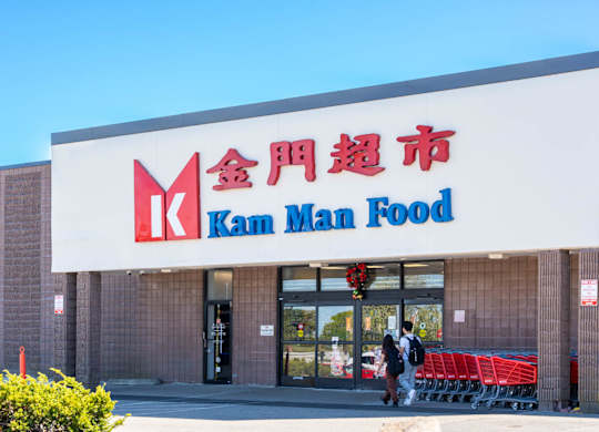A storefront of a Kam Man Food store with people walking by.