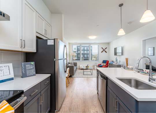 A kitchen with a black fridge and a white counter top A table with a book, a vase with reeds, and a lamp with a glowing bulb at the Mastlight.