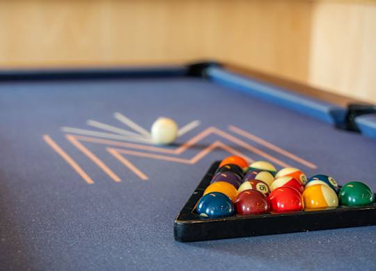A pool table at the Mastlight with a ball in motion and a rack of balls behind it.