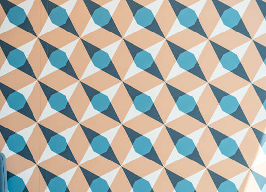 A geometric pattern of blue and peach shapes on a white background A table with a book, a vase with reeds, and a lamp with a glowing bulb at the Mastlight.