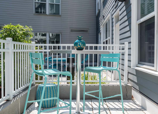 a small patio with blue chairs and a small table with a teal vase on it