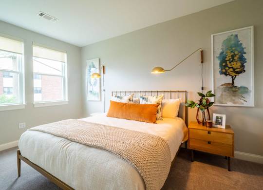 A cozy and well-lit living space that opens to a bedroom with soft furnishings and chic lighting.