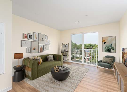 Furnished living room featuring an olive-green sofa, gallery-wall art and a large balcony door framing leafy suburban views.