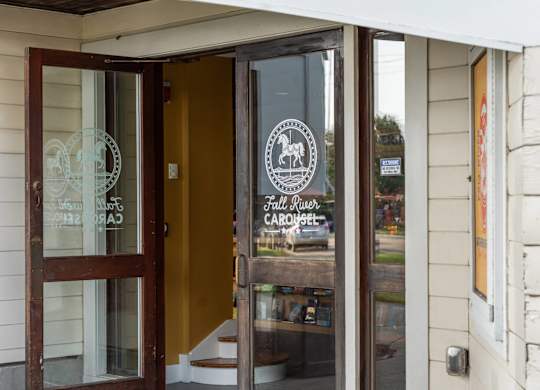 Close-up of the Fall River Carousel entrance door, featuring white horse logo etched on glass.