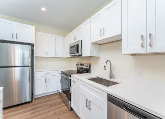 Close view of a white-quartz kitchen counter with undermount sink, gooseneck faucet and surrounding stainless appliances.