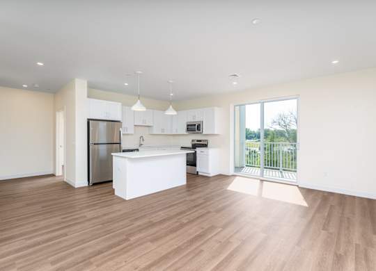 Open-concept living space combining island kitchen and lounge area, finished with wood-look flooring and a balcony door.