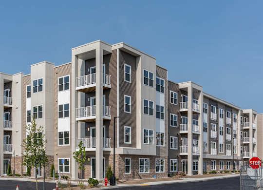 Four-story apartment building at Slade Farm Residences with mixed tan siding, stone base accents and multiple balconies.
