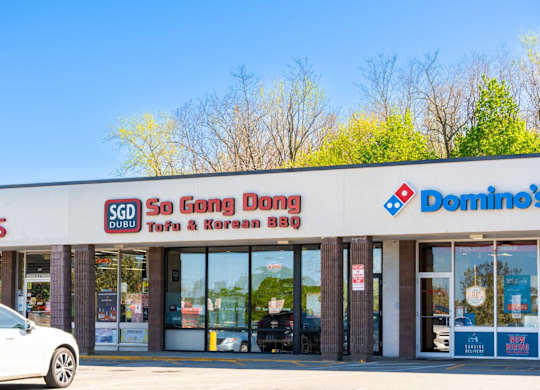 A white car is parked in front of a store with a sign that reads