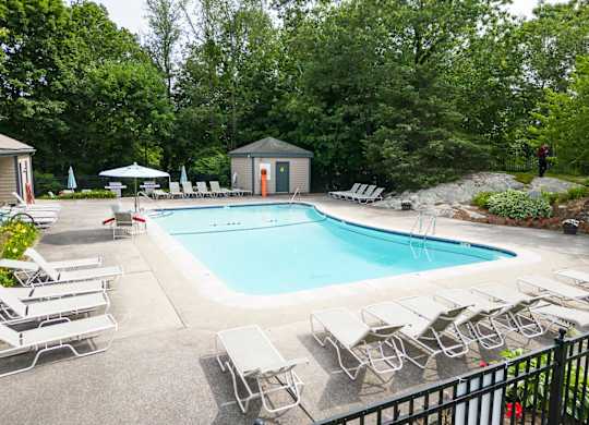 a swimming pool with chaise lounge chairs and trees in the background