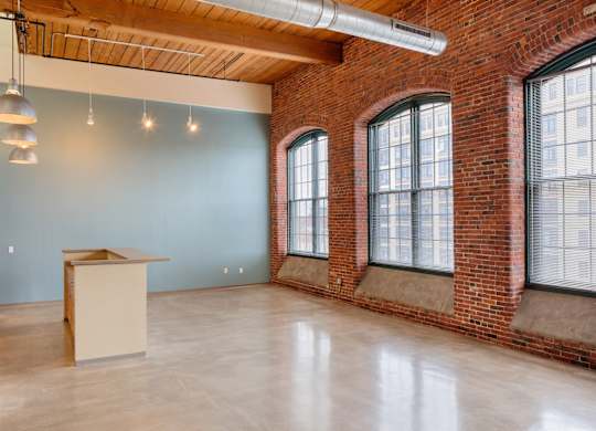 an empty room with three large windows and a desk in the corner