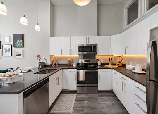 a kitchen with a large granite counter top and a sink, stainless appliances, electric range and sleek refrigerator