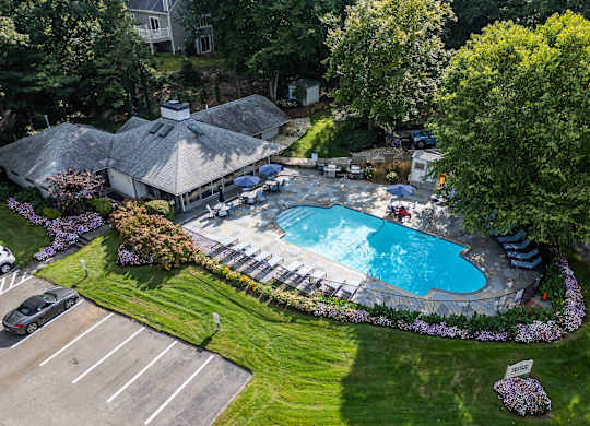an aerial view of a swimming pool in a backyard with a pavilion and lawn