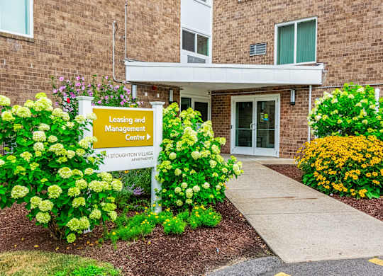 the front of a building with a loading and management center sign at North Stoughton Village, Massachusetts