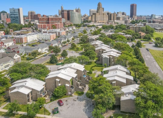 an aerial view of a cluster of houses with trees and a city skyline in the background