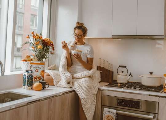 A woman is sitting on a kitchen counter with a dog beside her.