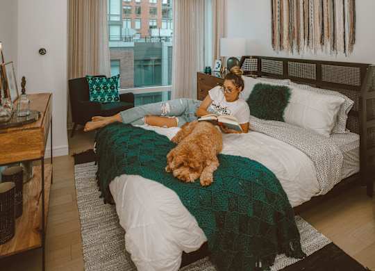 A woman is sitting on a bed with a dog on her lap.
