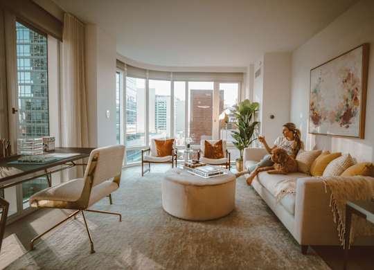 A woman is sitting on a couch in a living room with a large window and a view of the city.