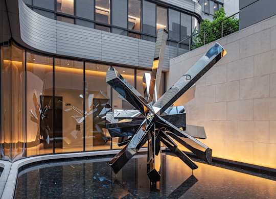 A large sculpture in front of a building with a glass facade.