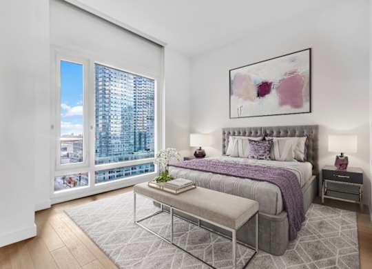 A bedroom with a large bed, a bench, and a window overlooking a cityscape.