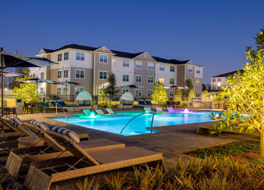 a swimming pool with lounge chairs and umbrellas in front of an apartment building at 55 Fifty at Northwest Crossing, Houston, TX 77092