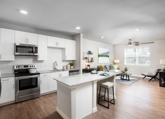 a kitchen and living room with white cabinets and stainless steel appliances at 55 Fifty at Northwest Crossing, Houston Texas
