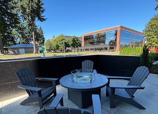 A chair and table are in the foreground with a building and trees in the background.