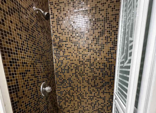 A shower with a brown tiled wall and a white floor.