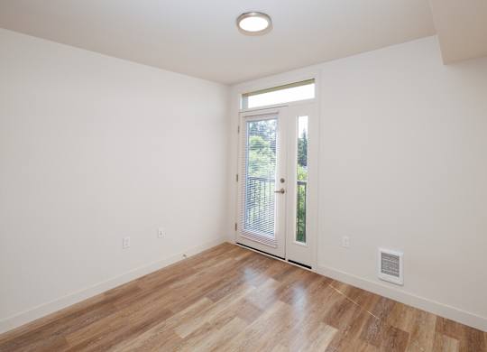A room with a wooden floor and a door leading outside.