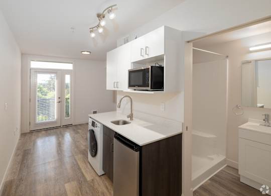 Modern kitchen with stainless steel appliances, white finishes, and open-concept living in our MFTE studio apartment homes
