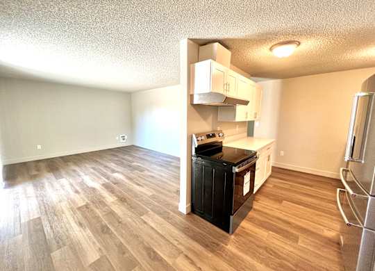 2-bedroom apartment kitchen and living room with a black stove, vinyl plank floors., and white cabinets
