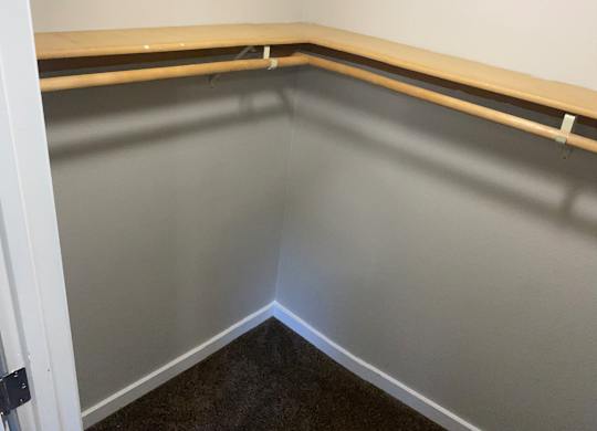 Large closet with white walls and bar to hang clothes in 1-bedroom apartment.